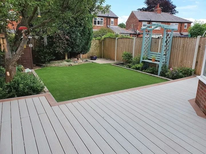 Grey composite decking area with artificial grass lawn and timber fencing in a completed garden makeover