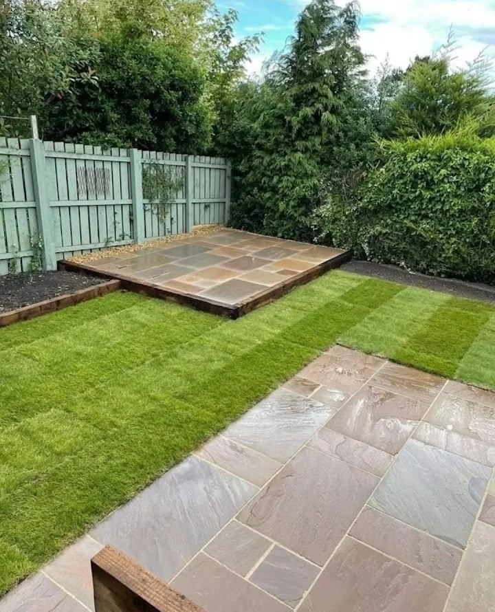 Newly laid Indian sandstone patio and striped turf lawn with timber sleepers in a landscaped family garden