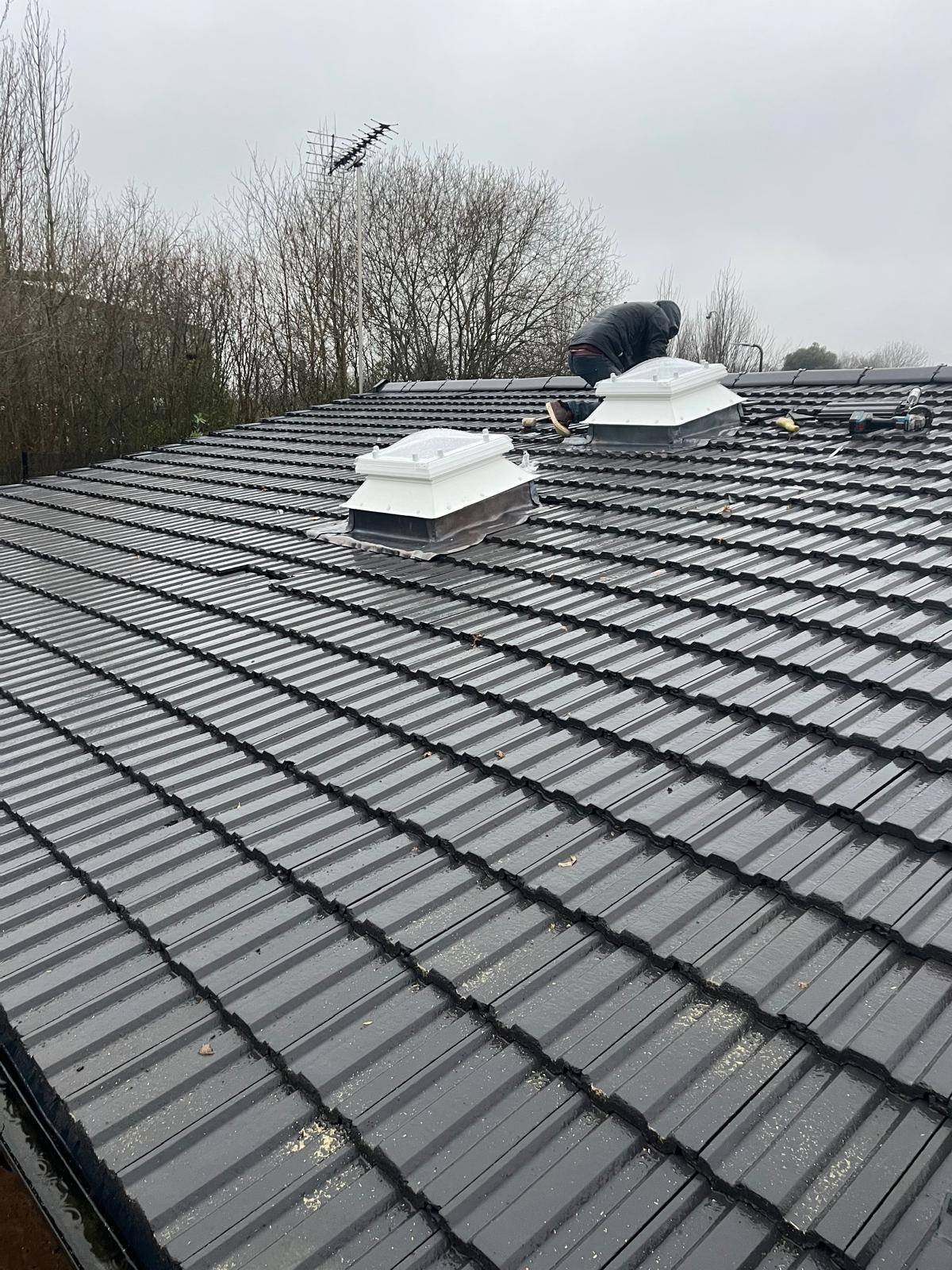Roofer fitting white roof window skylights into a grey tiled pitched roof during a re-roofing project